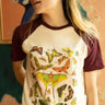 Woman wearing a cream and burgundy raglan tee featuring a vintage-style butterfly and moth illustration graphic by The Funnel Cake Tree
