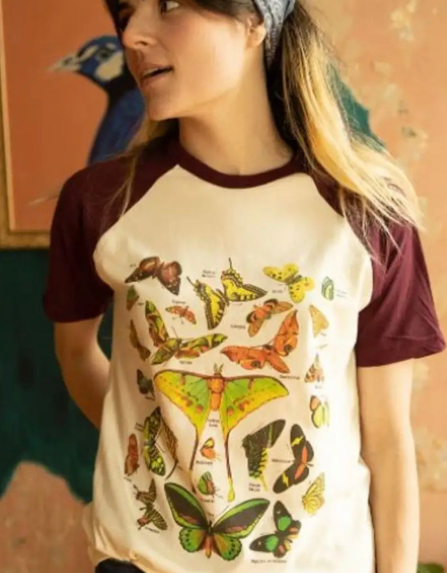 Woman wearing a cream and burgundy raglan tee featuring a vintage-style butterfly and moth illustration graphic by The Funnel Cake Tree