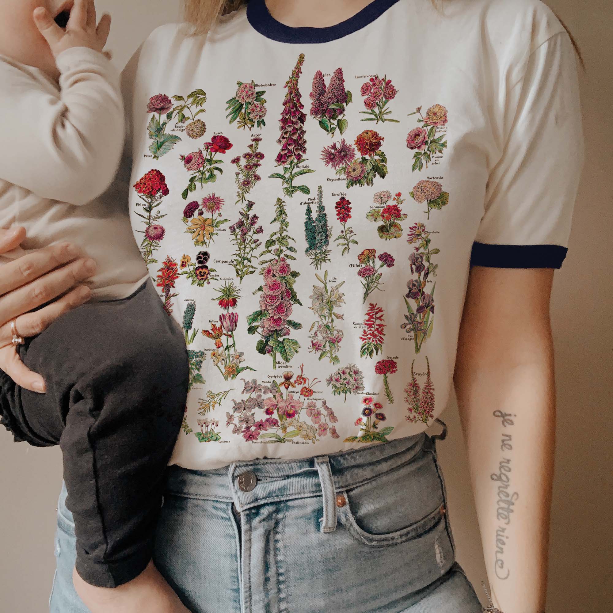 Woman wearing a cream and navy ringer tee featuring a colorful vintage-style wildflower illustration chart.