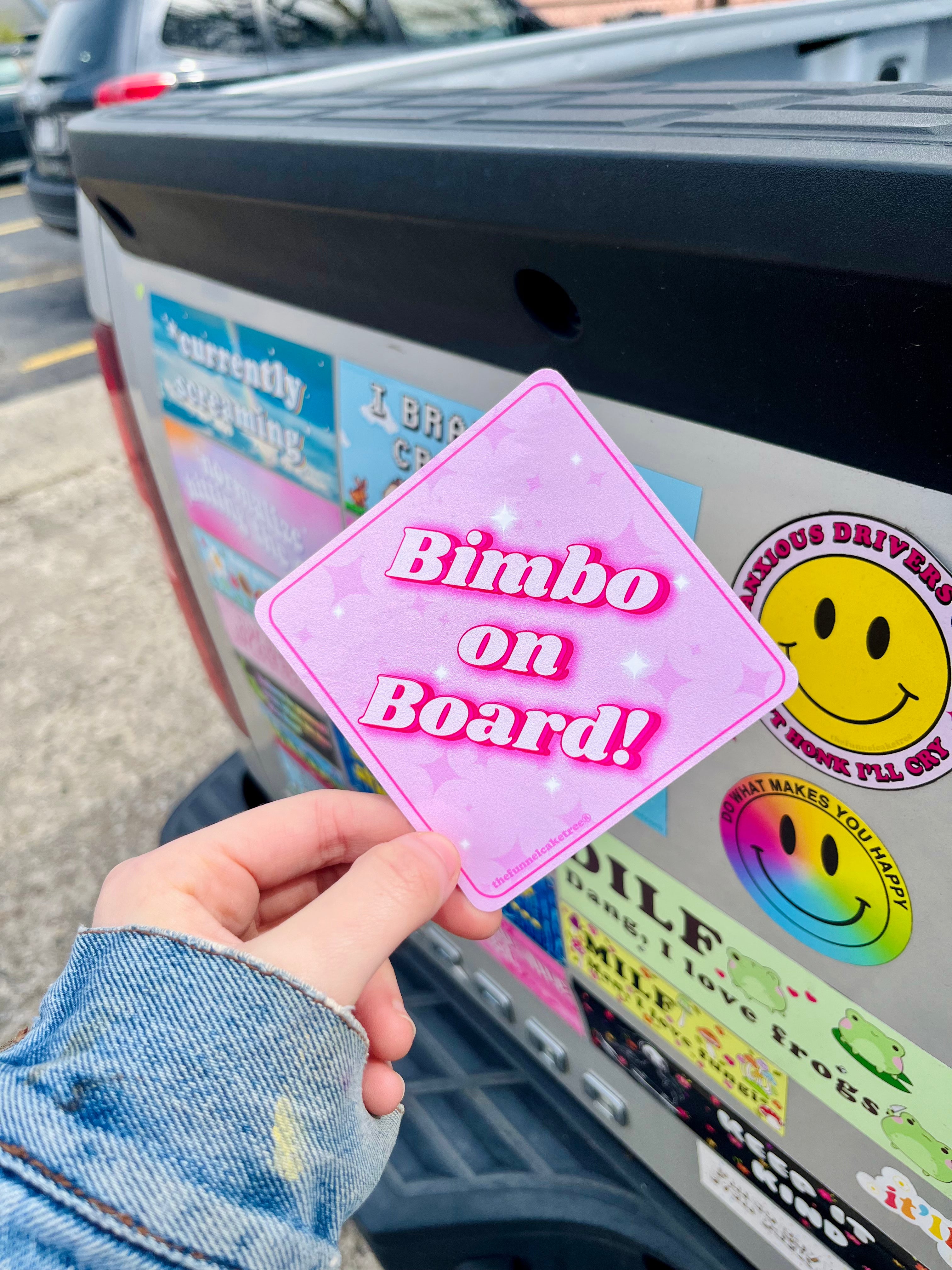 izzy from the funnel cake tree holding a diamond shaped pink sticker that says bimbo on board