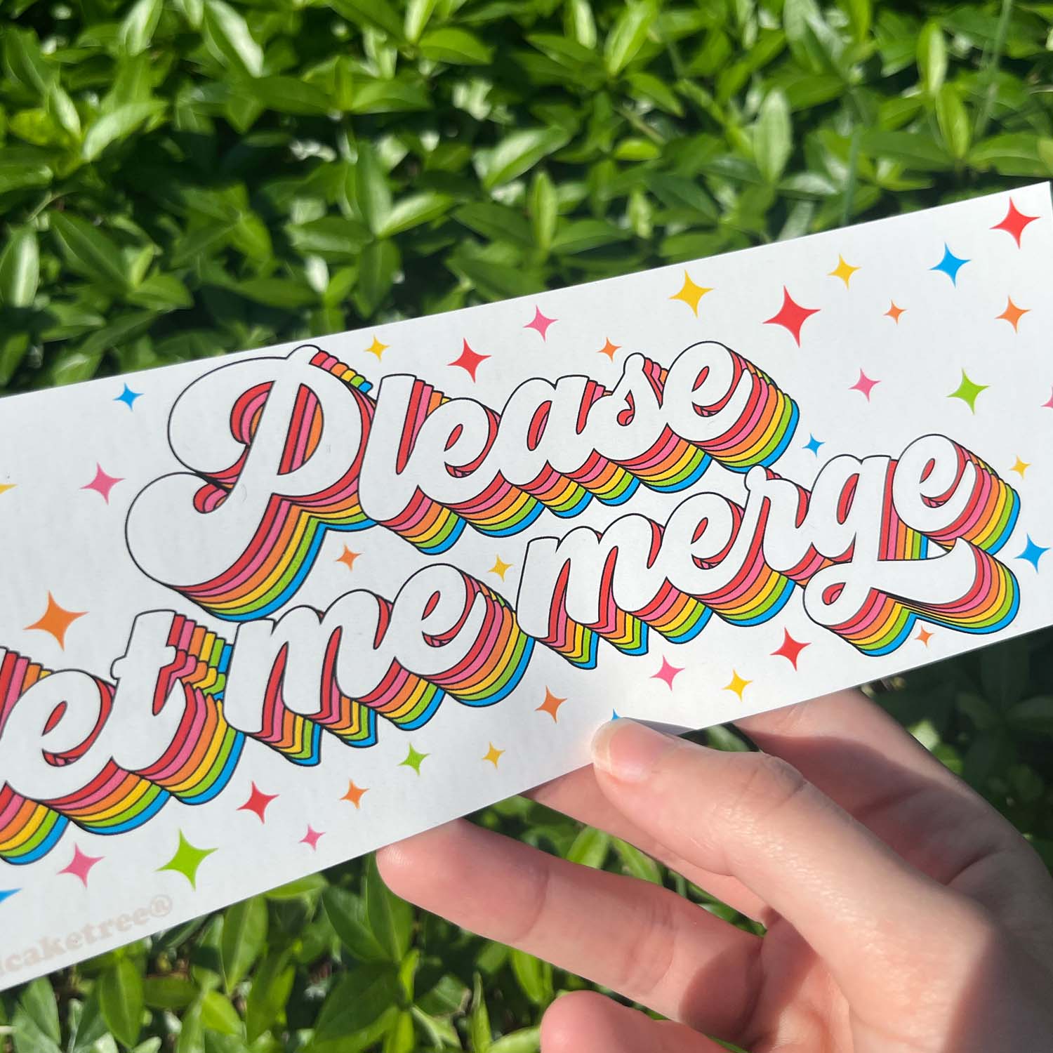 A hand holding a bumper sticker with the text 'Please let me merge' on it, featuring a colorful star pattern.