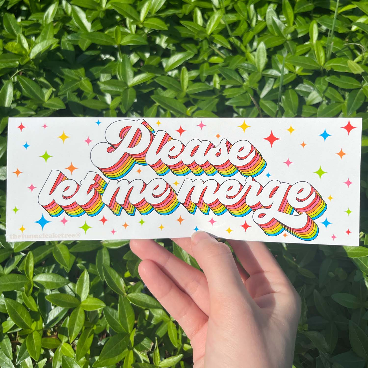 A hand holding a bumper sticker with the text 'Please let me merge' on it, featuring a colorful star pattern.