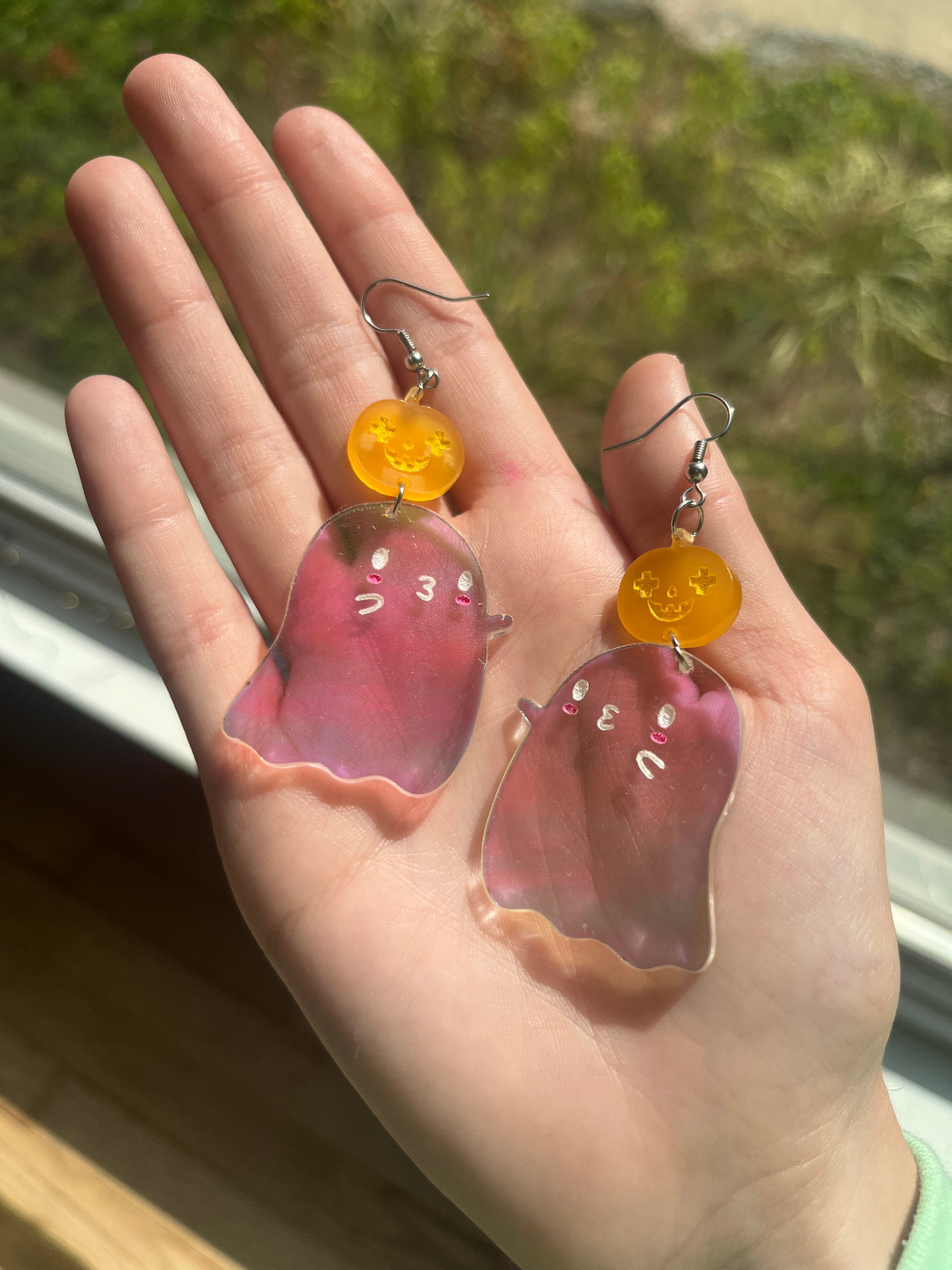 Izy with The Funnel Cake Tree holding acrylic ghost shaped earrings that also have a jack o latern on them