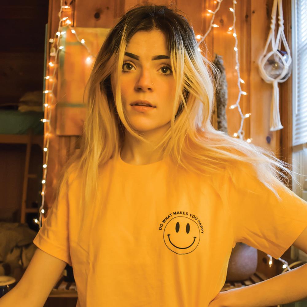 Person wearing yellow ‘Do What Makes You Happy’ graphic tee by Funnel Cake Tree featuring a minimalist black smiley face design  cheerful positive vibes t-shirt.