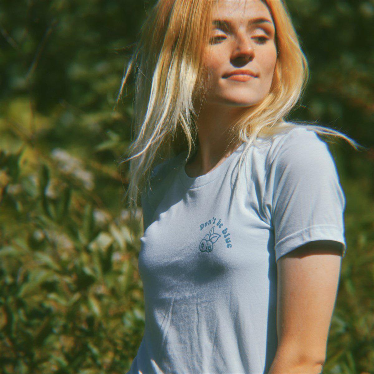 Light blue ‘Don’t Be Blue’ graphic tee by Funnel Cake Tree featuring a minimalist blueberry design and uplifting message, photographed outdoors in natural light.