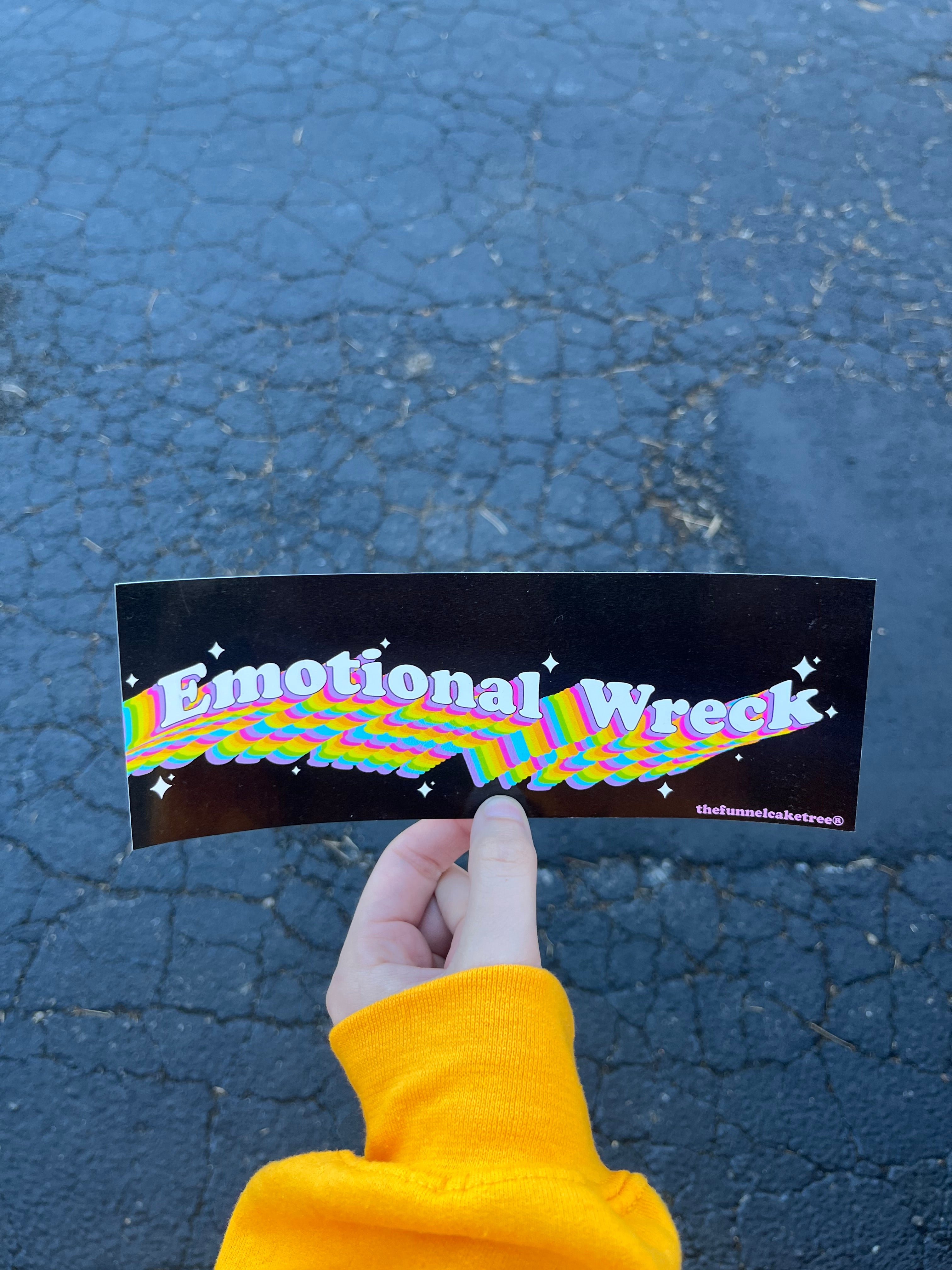 Glossy black bumper sticker with bold rainbow 3D text reading “Emotional Wreck” with sparkles and colorful wave accents.