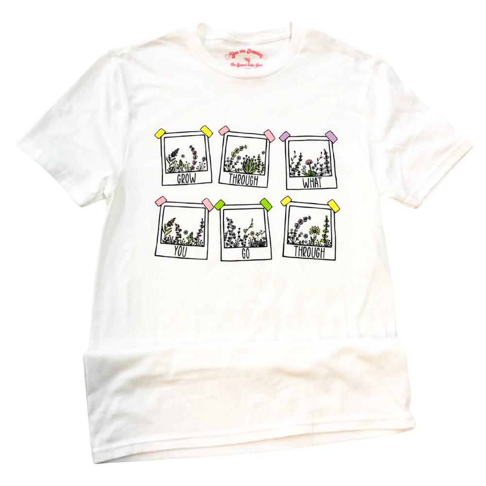 Grow Through What You Go Through flat lay graphic tee by Funnel Cake Tree white unisex t-shirt featuring six pastel polaroid-style floral frames with positive lettering, displayed neatly on a flat surface.
