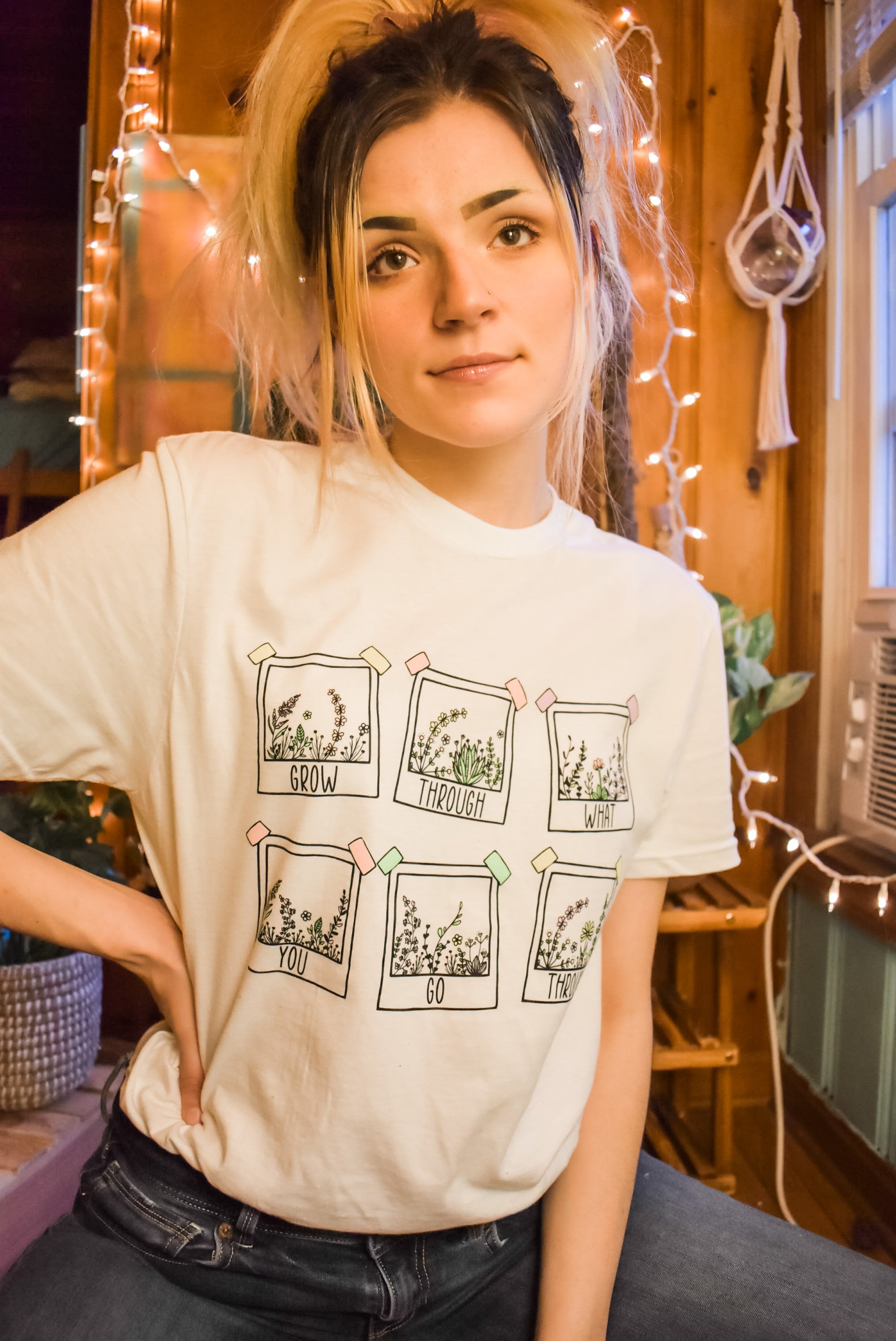 Grow Through What You Go Through lifestyle graphic tee by Funnel Cake Tree  cream unisex t-shirt featuring six hand-drawn floral frames and inspirational lettering, modeled indoors with cozy string lights.