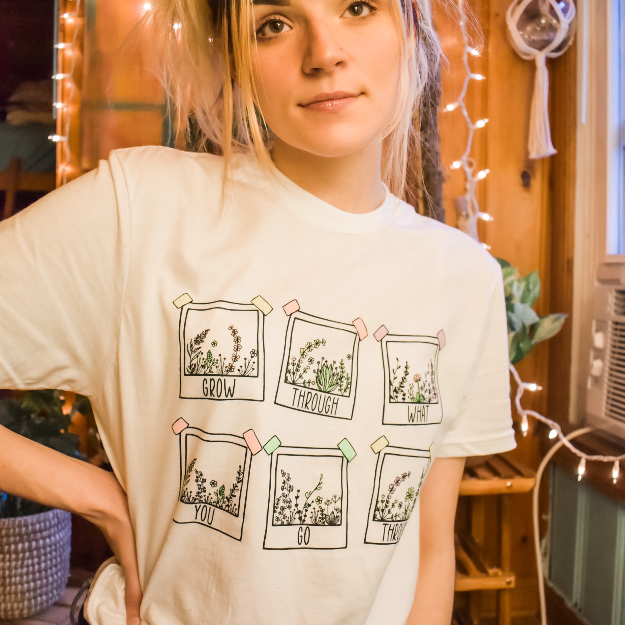 Grow Through What You Go Through lifestyle graphic tee by Funnel Cake Tree  cream unisex t-shirt featuring six hand-drawn floral frames and inspirational lettering, modeled indoors with cozy string lights.