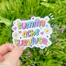 Pastel rainbow die-cut vinyl sticker reading “Tummy Ache Survivor” with hearts, stars, and smiley daisies.