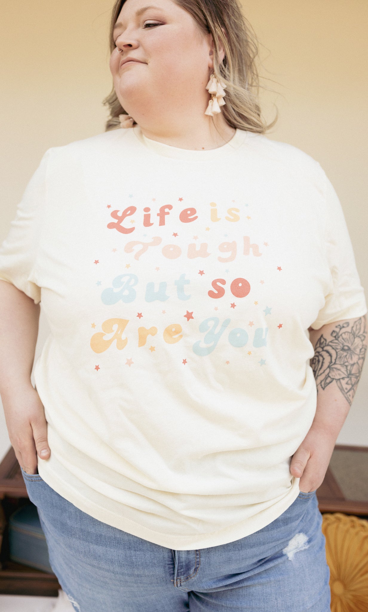 Close-up of cream ‘Life is Tough But So Are You’ graphic tee showing colorful retro typography and soft cotton texture.