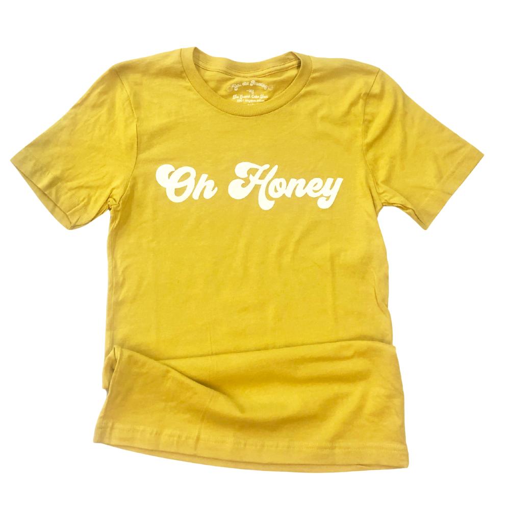 Flat lay of a yellow ‘Oh Honey’ graphic tee with white retro lettering, styled for a vintage-inspired look.