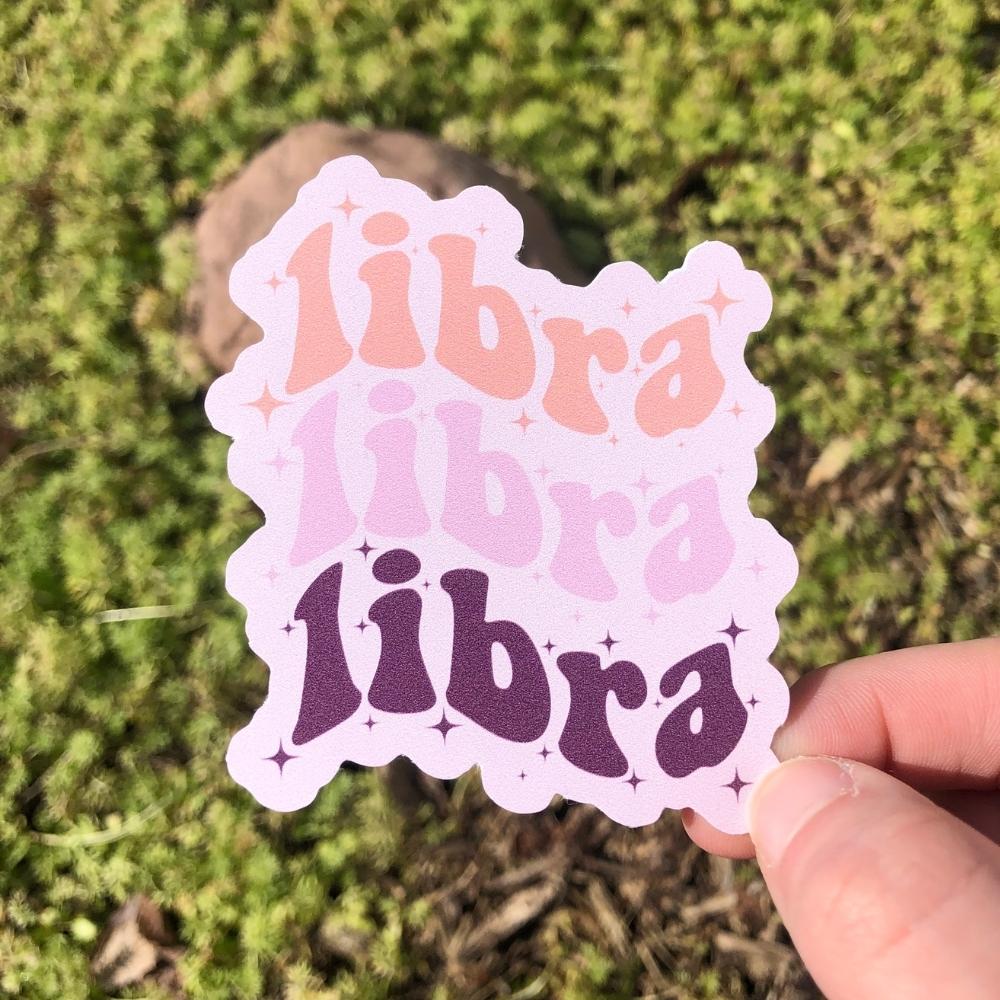 Izy from The Funnel Cake Tree holding a purple pink and peach sticker with the word libra repeating on it