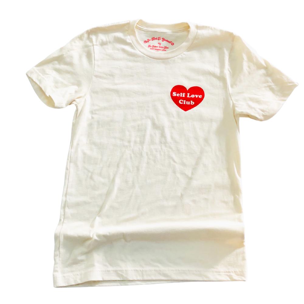 Cream Self Love Club graphic tee with a red heart design and minimalist text, laid flat on a white background, perfect for casual, empowering everyday wear.