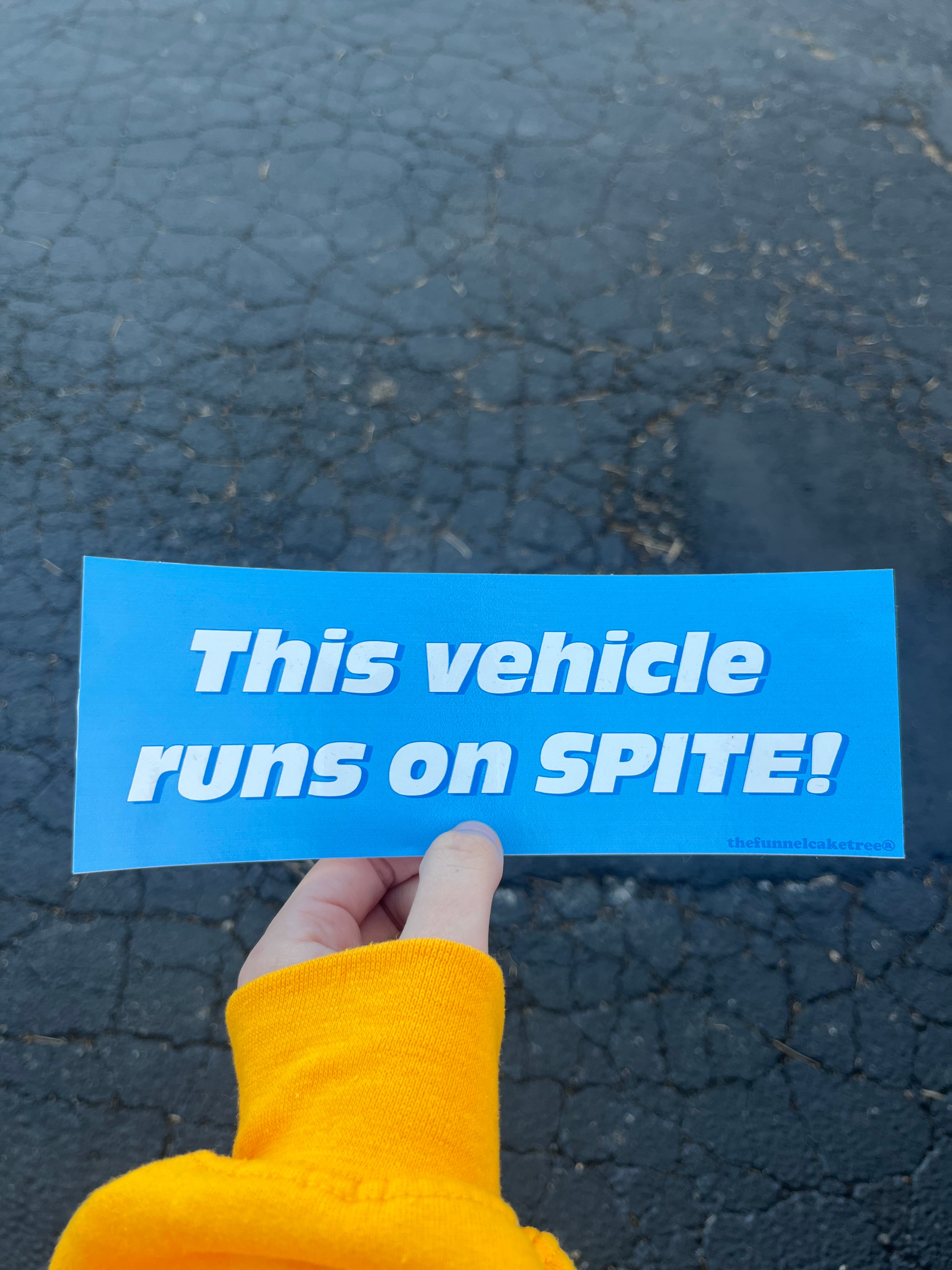 Glossy bright blue bumper sticker with bold white and blue text reading “This vehicle runs on spite!”