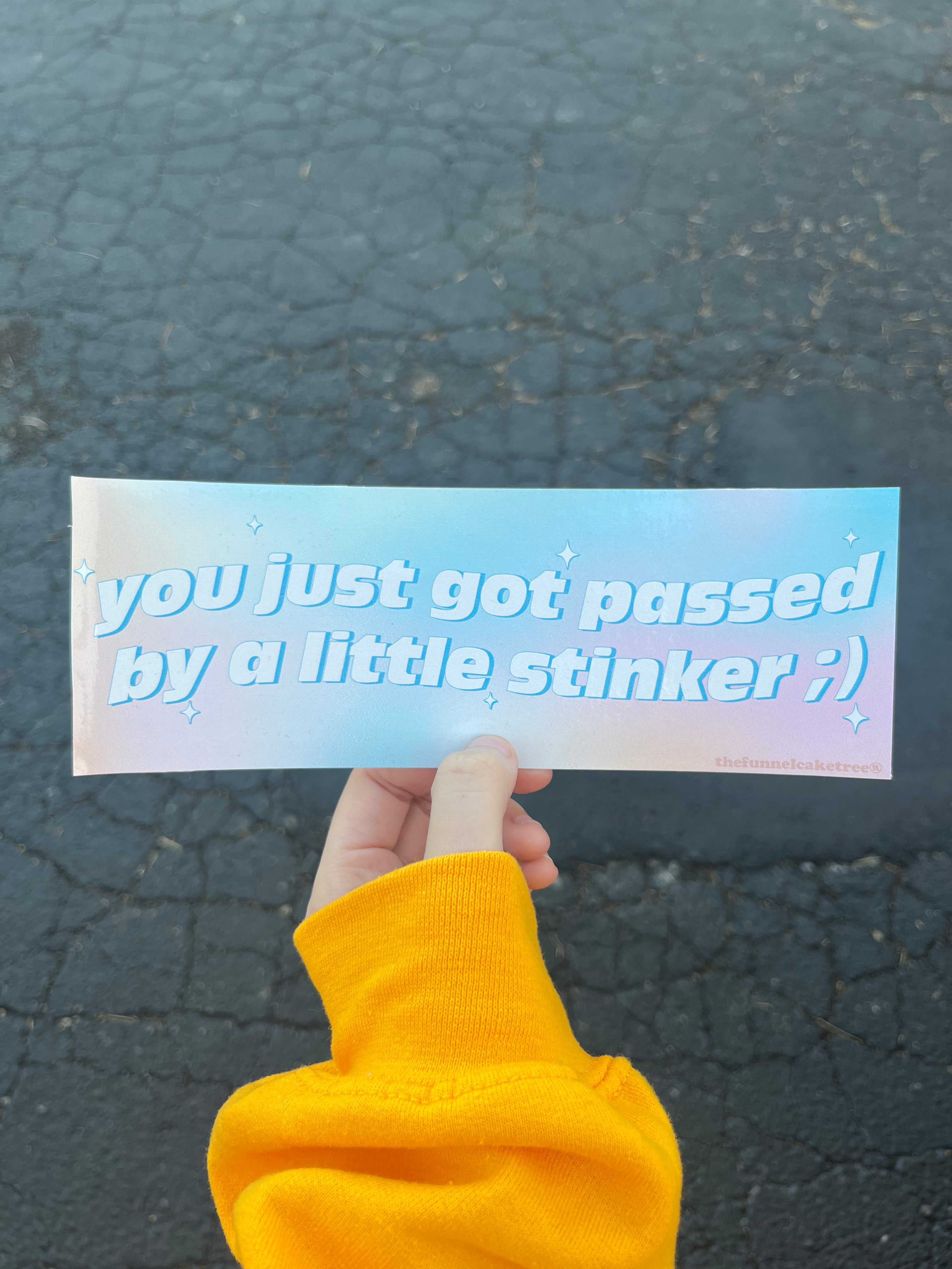 Glossy pastel blue and pink bumper sticker with white text reading “you just got passed by a little stinker ;)” accented with sparkles.